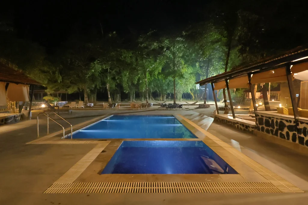 Luxury jungle resort swimming pool at night surrounded by forest in Madhya Pradesh