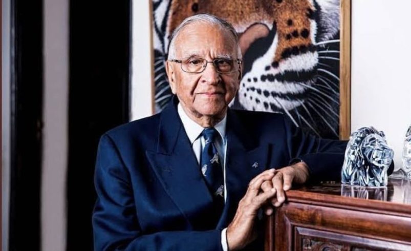 "Dr. M. K. Ranjitsinh, pioneer of wildlife conservation in India, standing in front of a tiger portrait"